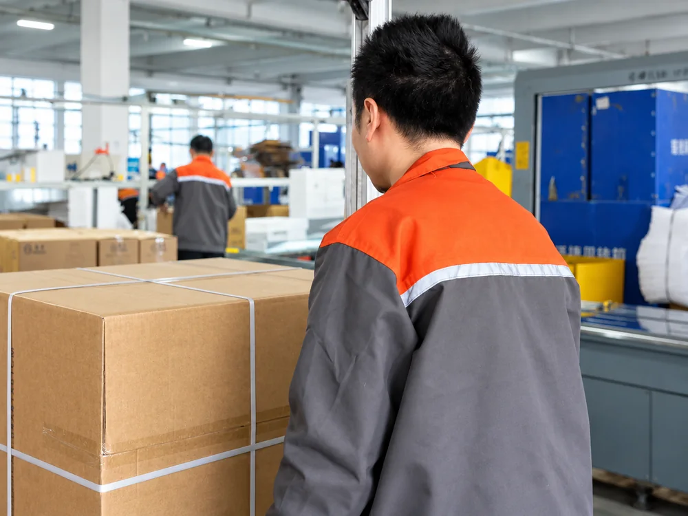 Factory worker beside a strapped shipping carton and packing conveyor