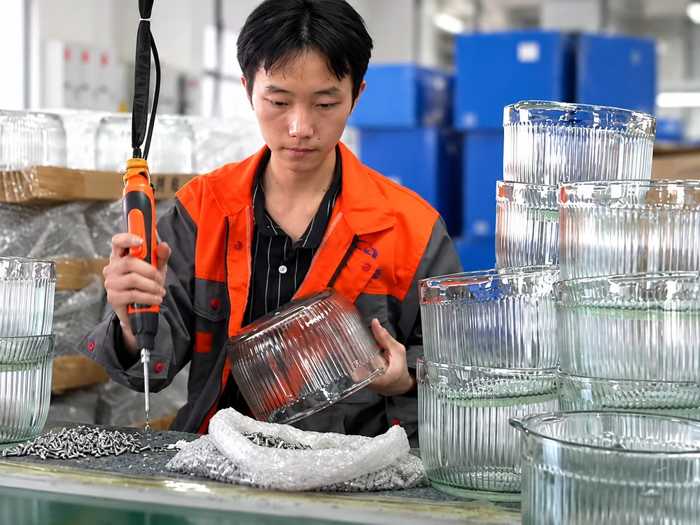 Factory worker handling a glass bowl beside other glass bowls at a workbench