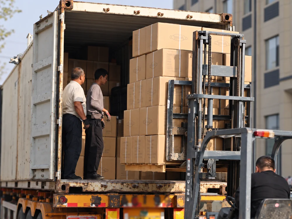 Cartons at an open shipping container with loading staff and a forklift mast