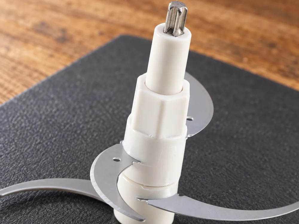Close view of a white chopper blade shaft, metal coupling and curved blades on a review mat
