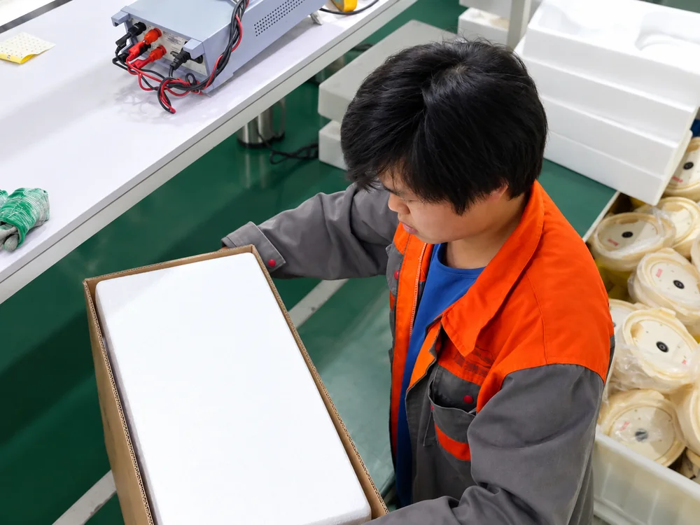 Factory worker handling a carton with a white protective insert at a workbench
