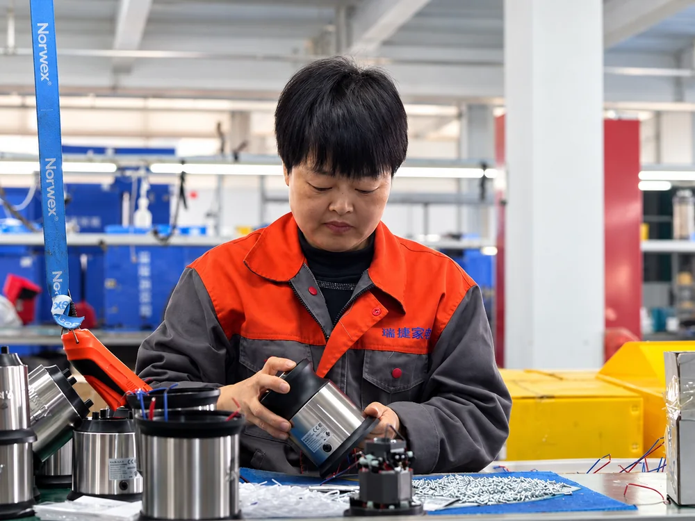 A worker handling a motor housing at a JINJIE assembly workstation