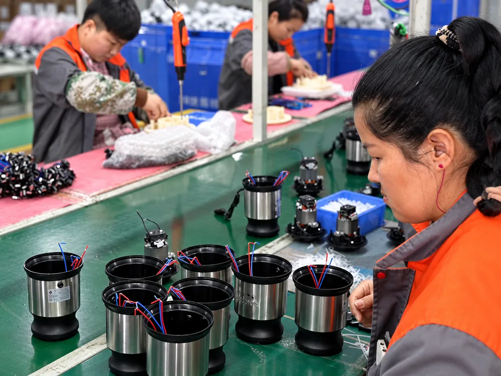 Motor housings and components beside workers at JINJIE assembly workstations