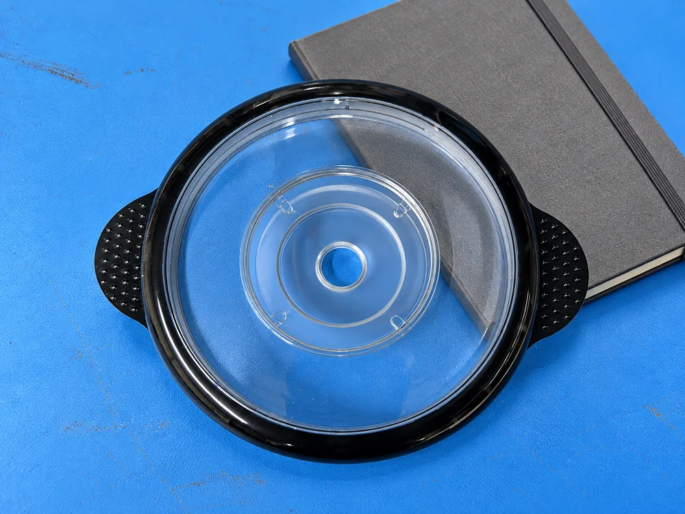 Transparent chopper lid with a black rim beside a closed notebook