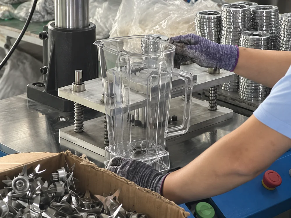Close view of gloved hands and a blender jug at an assembly fixture