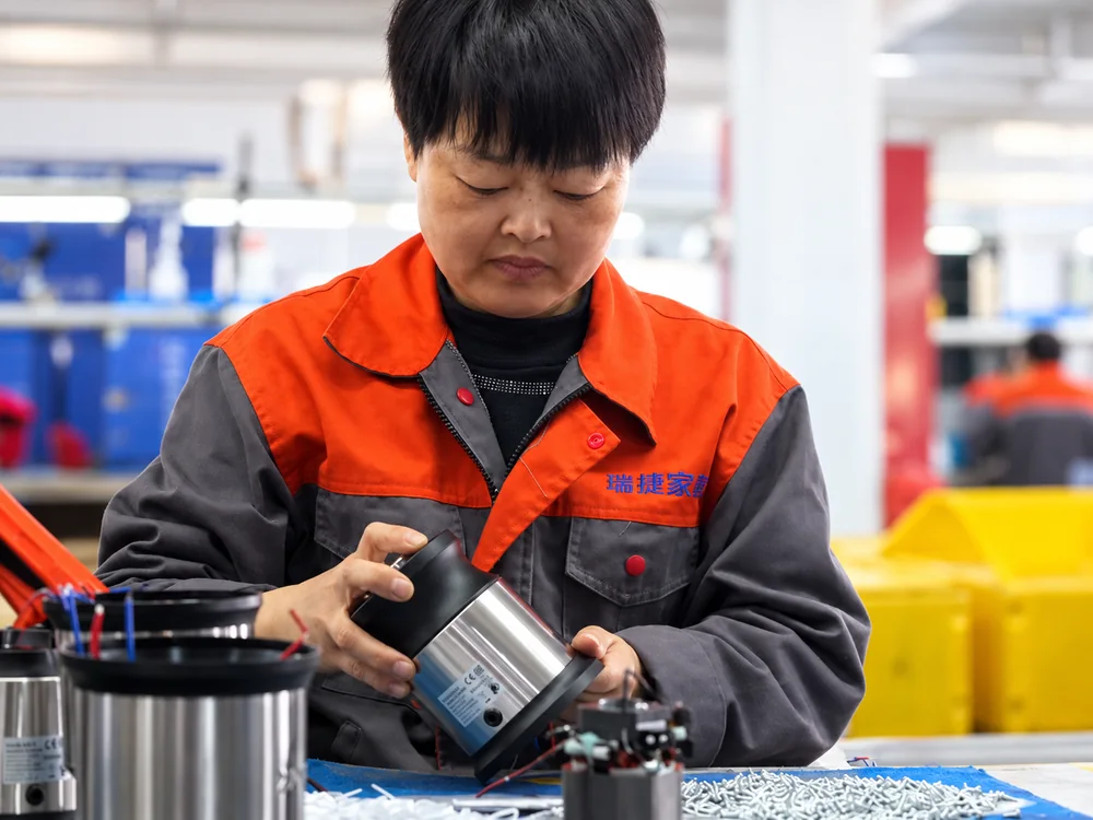 Worker handling a metal motor housing and its black components at an assembly bench