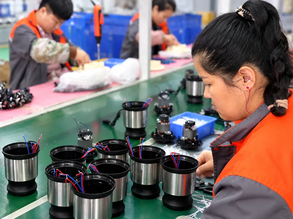 Worker handling steel and black appliance housings beside an assembly conveyor