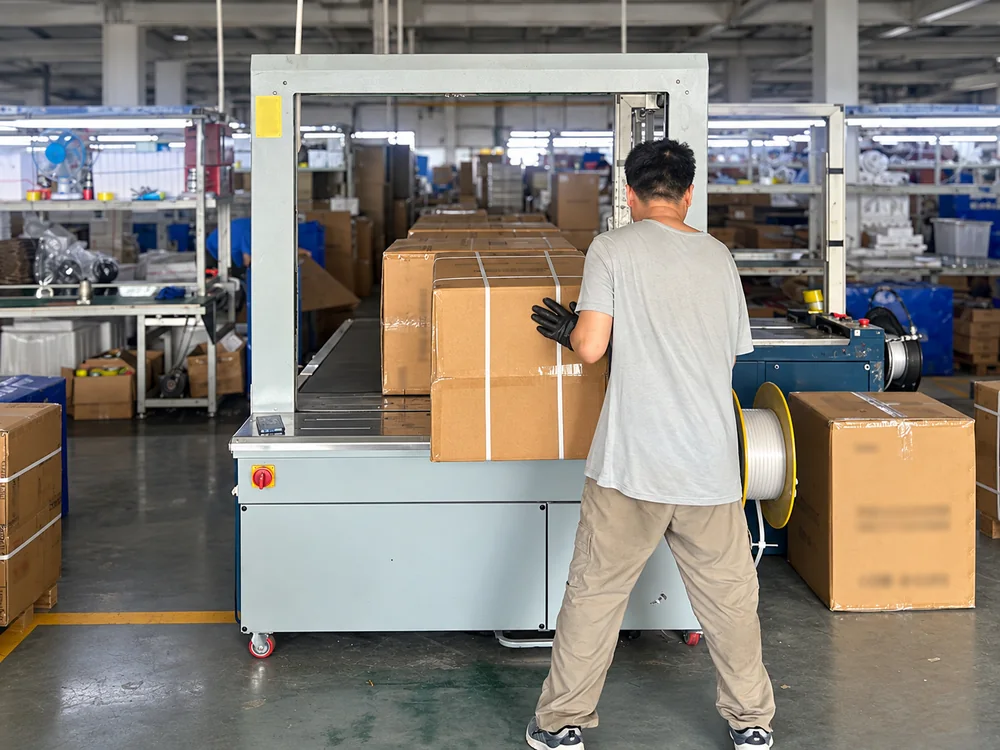 Worker handling a carton at a real appliance packing station with customer details blurred